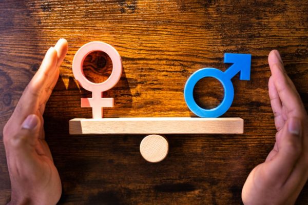Simboli di genere femminile e maschile in equilibrio su una bilancia di legno, con mani a protezione